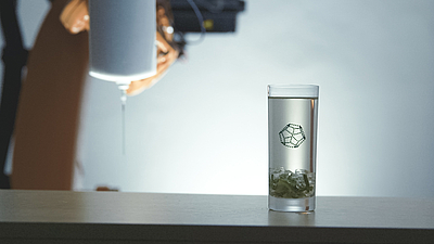 Ein Wasserglas steht auf einem Tisch. Darin befindet sich ein 3-D-Druck aus feinen Tropfen Speiseöl